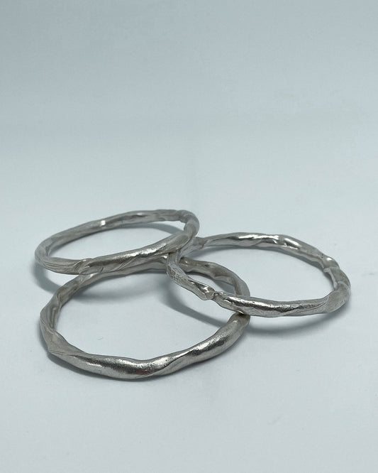 3 heavy organic round Fine Silver Bangles lying in a pile on a flat surface
